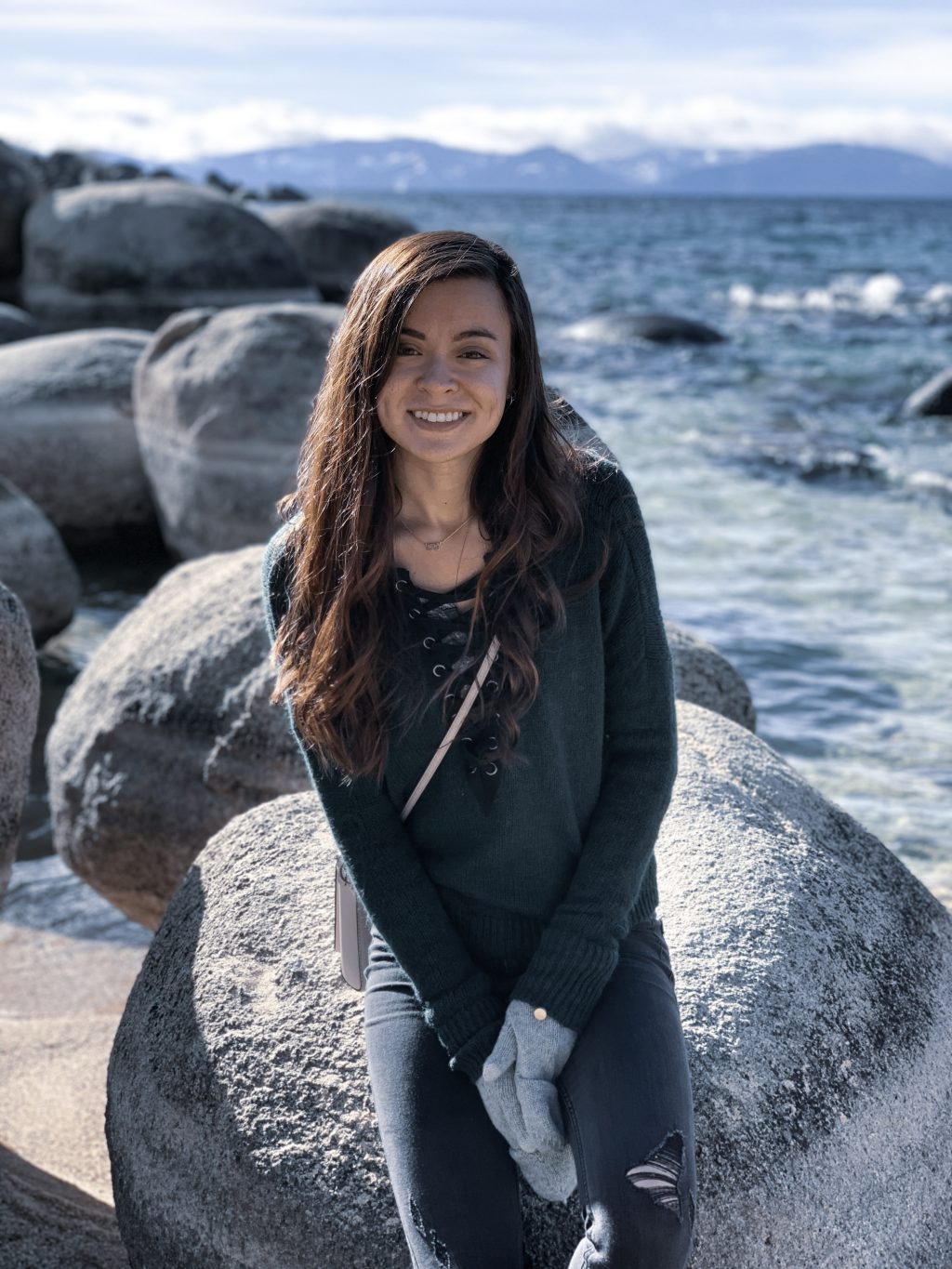 a woman sitting on a rock by the water