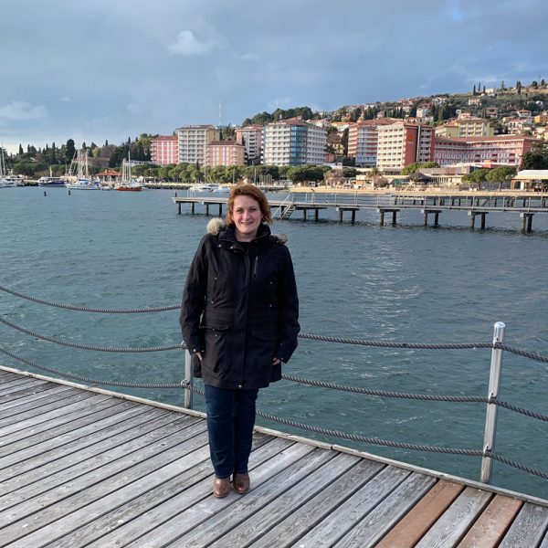 a woman standing on a dock with a body of water and buildings in the background