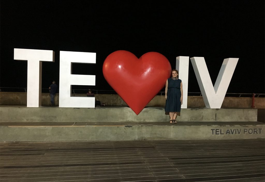 a woman standing in front of a large white sign with a large red heart