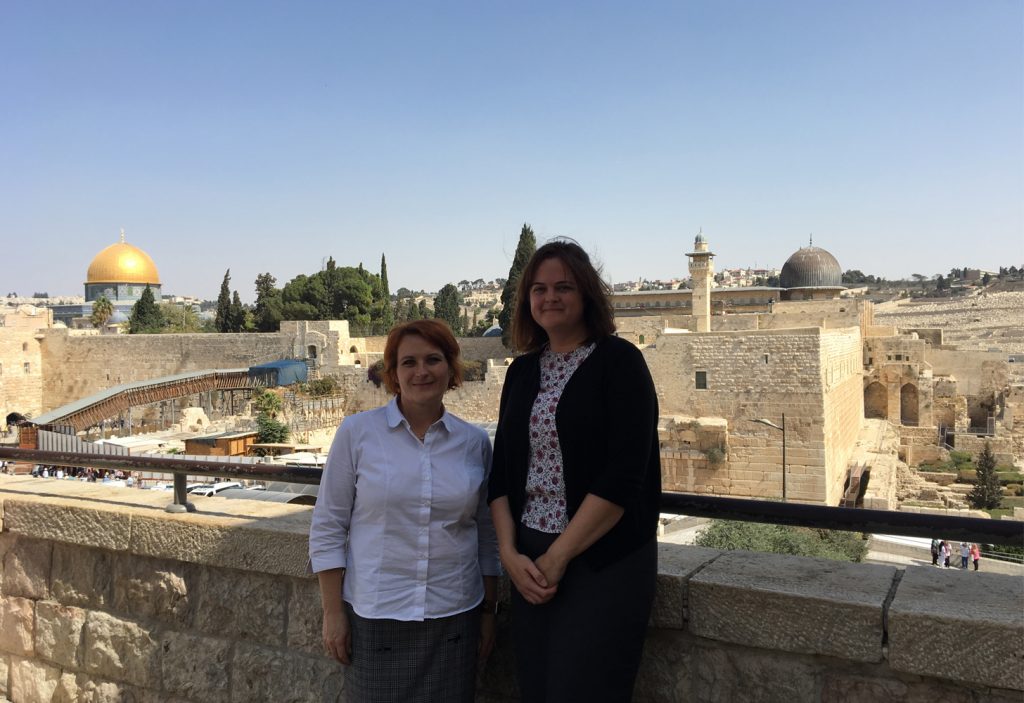 two women standing on a ledge with a city in the background