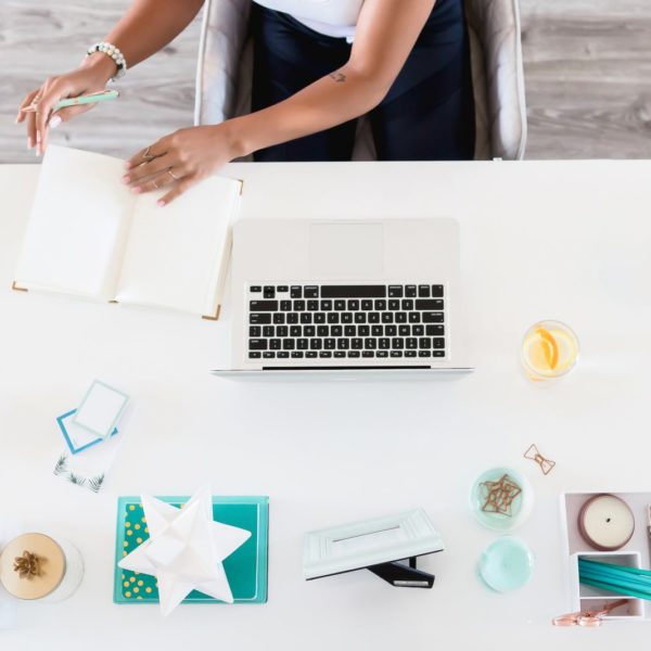 Cover Photo of woman in front of laptop flipping through notebook for How to Travel More With a Full Time Job