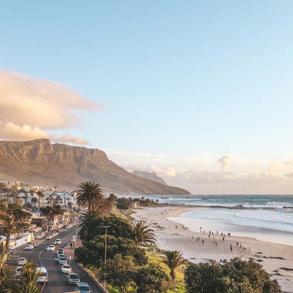 a beach with a road and buildings and mountains in the background