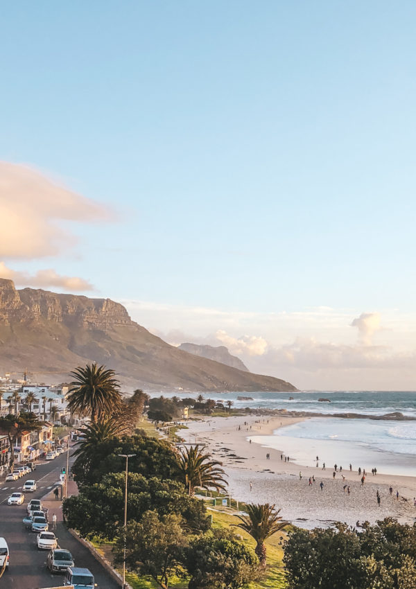 a beach with a road and buildings and mountains in the background