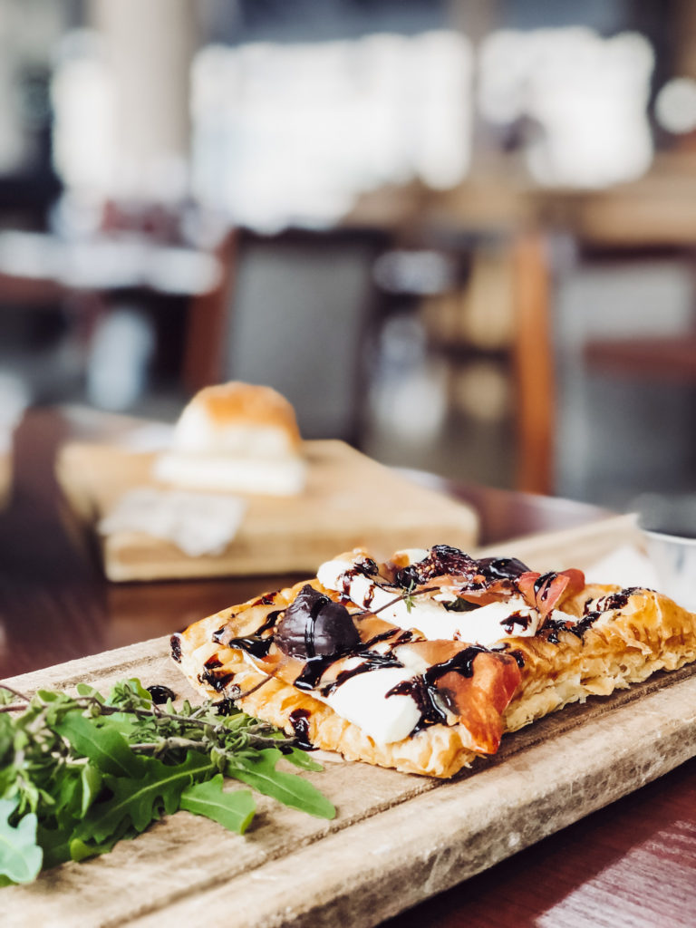 a square pastry with toppings and sauce on a wooden board