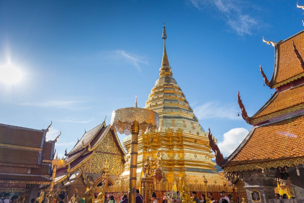 a large gold pagoda with people walking around with Wat Phra That Doi Suthep in the background