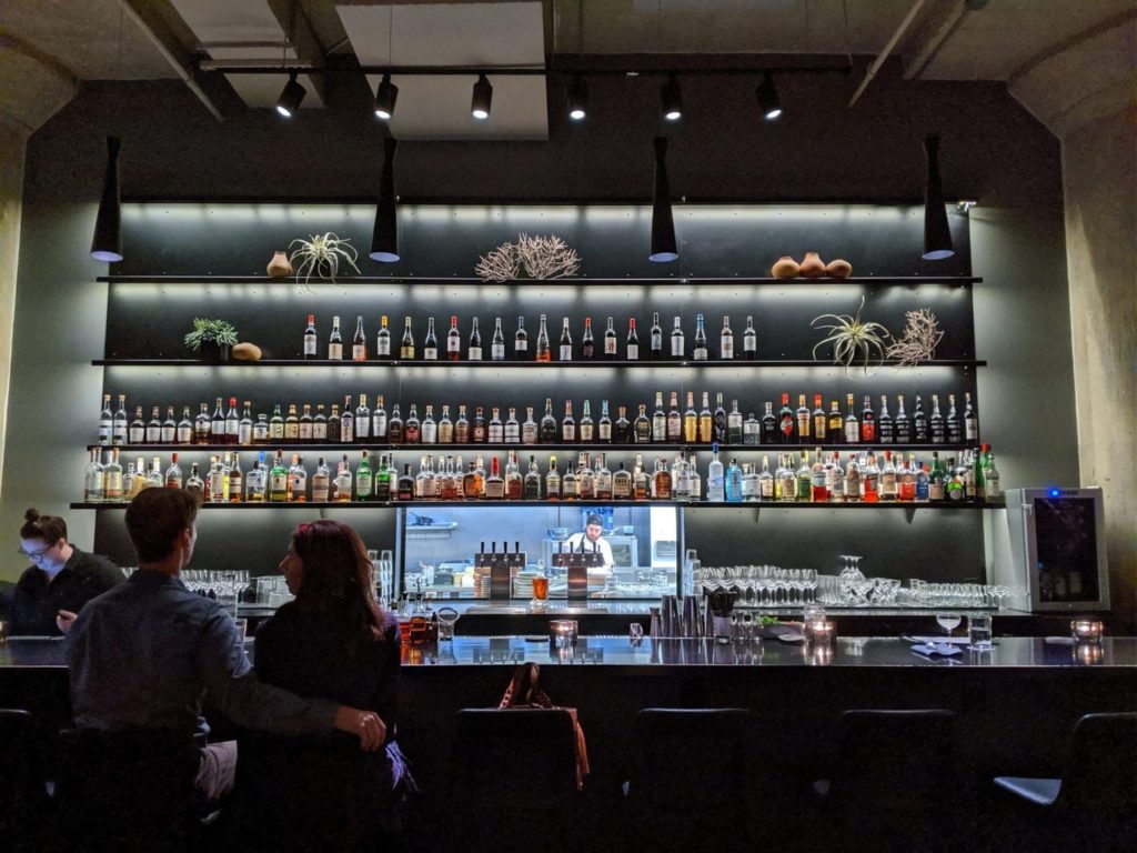 a man and woman sitting at a bar with bottles on shelves