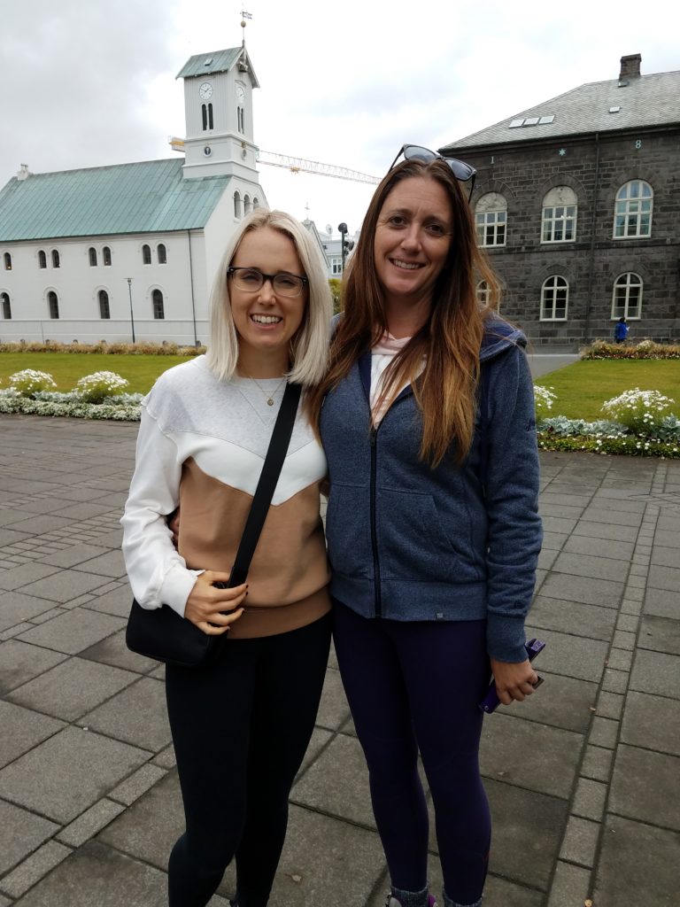 two women standing together in front of a building