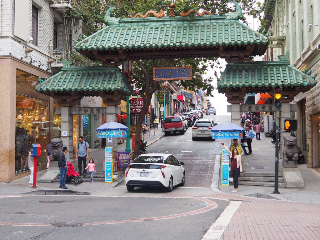 a street with cars and people walking around with Chinatown in the background